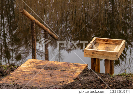 A wooden ramp leads to a platform near a calm pond surrounded by trees, capturing the peacefulness of early morning 133861974