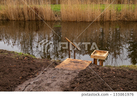 Steps made of wood go down to a still pond with reflections of trees, creating a peaceful scene in a natural setting 133861976