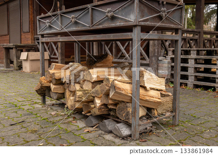 A metal rack holds neatly arranged wooden logs next to a rustic wooden building surrounded by fallen leaves in a quiet forest A metal rack holds neatly arranged wooden logs next to a rustic wooden building surrounded by fallen leaves in a quiet forest 133861984