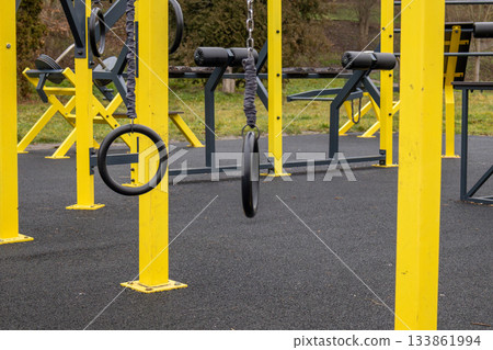 Bright yellow workout equipment stands in a fitness area, showcasing gym rings ready for various exercises in a grassy park setting 133861994