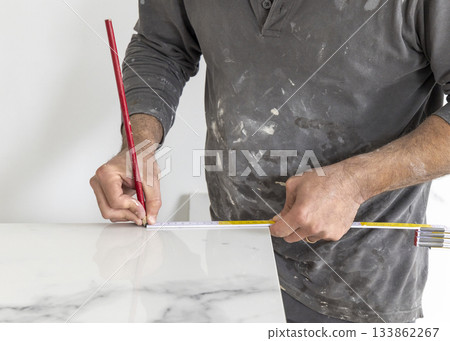 Craftman in grey shirt measures a marble tile using a ruler. Handy men at work, hands closeup Craftman in grey shirt measures a marble tile using a ruler. Handy men at work, hands closeup 133862267