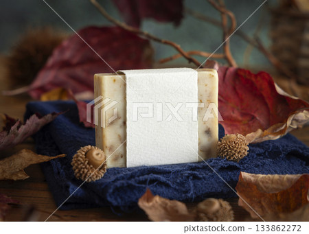 Soap bar with blank label on blue cloth near autumn dried leaves, twigs and acorns, mockup 133862272