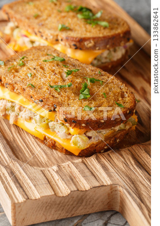 Tuna melt is a sandwich made of bread, tuna and cheese with added vegetables and mayonnaise, close-up on a wooden board. Vertical 133862641