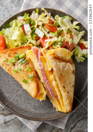 One-Pan Egg Toast with ham and gooey melted cheese served with fresh salad closeup on the plate on the table. Vertical top view One-Pan Egg Toast with ham and gooey melted cheese served with fresh salad closeup on the plate on the table. Vertical top view 133862647