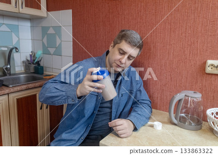 Man preparing a protein shake in a kitchen, measuring powder into a shaker for fitness, recovery, and muscle health. 133863322