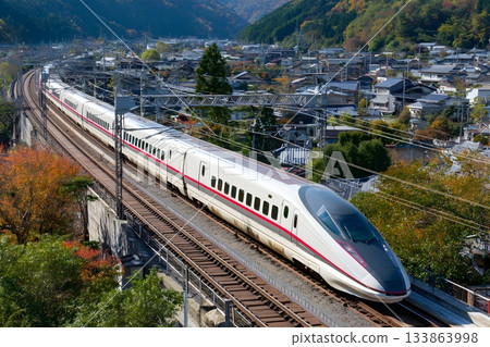 A modern train speeds along tracks through a scenic countryside. 133863998