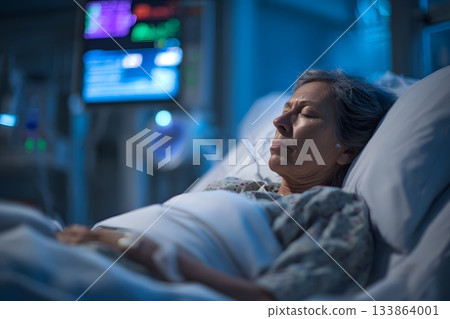 A patient rests in a hospital bed near a medical monitor. 133864001