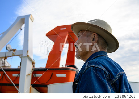A senior man wearing a hat is seen on the deck of a ship 133864265