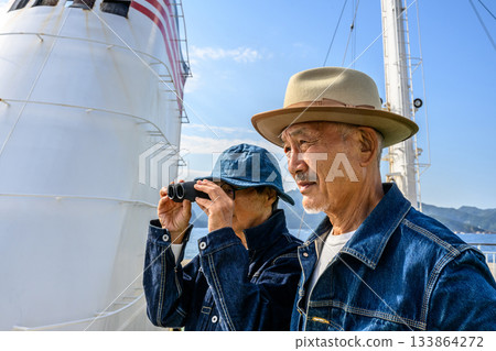 Senior couple looking at the scenery through binoculars, enjoying a boat trip 133864272