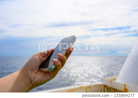 Hand holding a smartphone on a ship Hand holding a smartphone on a ship 133864277