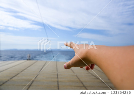 A hand on a boat points towards the blue sea and sky A hand on a boat points towards the blue sea and sky 133864286
