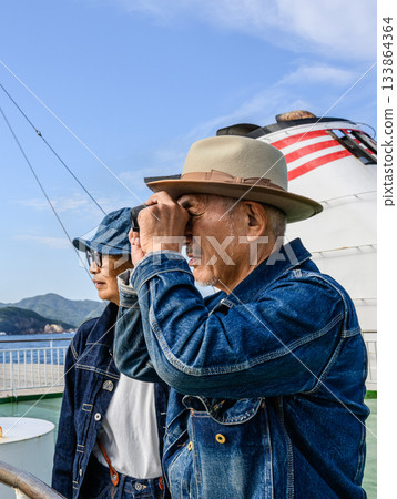 A denim-clad woman peering through binoculars at the view A denim-clad woman peering through binoculars at the view 133864364