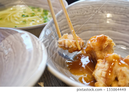 Chopsticks picking up crispy fried chicken coated in sweet sauce from bowl Chopsticks picking up crispy fried chicken coated in sweet sauce from bowl 133864449