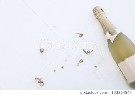 Celebration champagne bottle in snow with gold star confetti, party streamers. Festive winter holiday background for New Year. Christmas party decor. Elegant seasonal concept. Flat lay, top view Celebration champagne bottle in snow with gold star confetti, party streamers. Festive winter holiday background for New Year. Christmas party decor. Elegant seasonal concept. Flat lay, top view 133864544