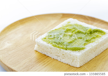 A single slice of white bread with a spread of Pandan Custard is placed on a round wooden plate, showcasing simple and natural 133865585