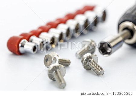Close-up of silver metal screws with a socket wrench attachment and a row of socket bits with red holders on a white background 133865593