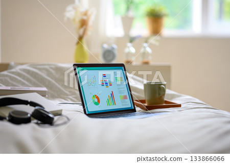 在床上用筆記型電腦進行數據分析，同時喝著飲料。 133866066