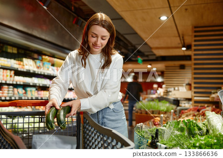 A woman pushes a cart full of vegetables in a grocery store A woman pushes a cart full of vegetables in a grocery store 133866636