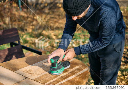 Man sanding wooden garden table with sander 133867091