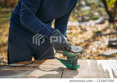 Man polishing wooden table surface with orbital sander during renovation 133867098