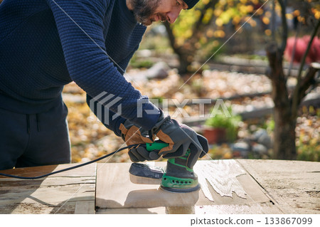 Man polishing wooden table surface with orbital sander during renovation 133867099