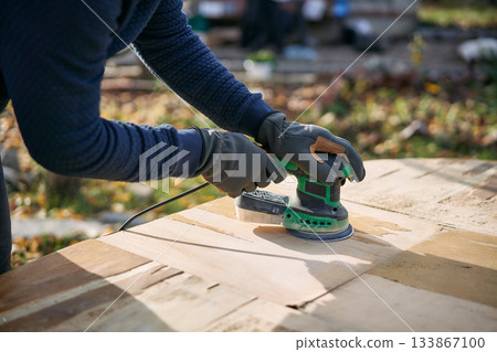 Man polishing wooden table surface with orbital sander during renovation 133867100