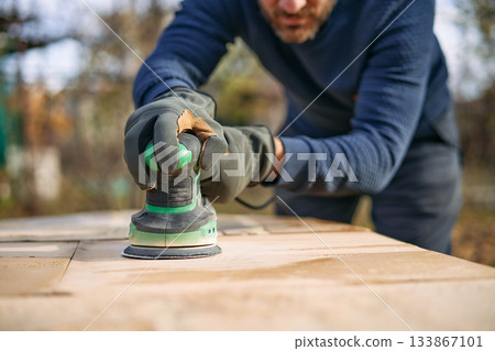 Man polishing wooden table surface with orbital sander during renovation 133867101