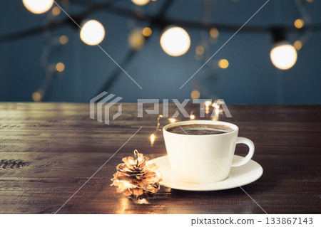 Cup of black coffee on wooden board in cafe. Blurred gold garland and pine cone as background. Christmas Time. Image for display or montage your products. 133867143