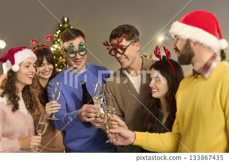 Young friends toasting champagne at home Christmas party, wearing festive hats Young friends toasting champagne at home Christmas party, wearing festive hats 133867435