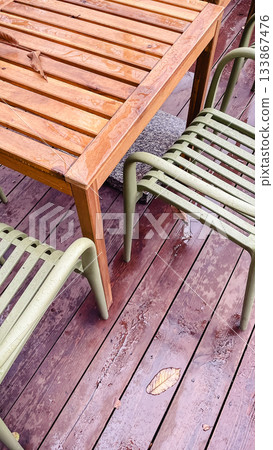 Wet wooden table and olive green metal chairs on a dark deck with fallen leaves after a rain shower 133867476