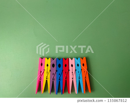 The image shows a row of colorful wooden clothespins on a green background. The image shows a row of colorful wooden clothespins on a green background. 133867812