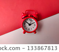 The small red analog alarm clock on a white and red background. 133867813
