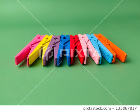 The image shows a row of colorful wooden clothespins on a green background. The image shows a row of colorful wooden clothespins on a green background. 133867817