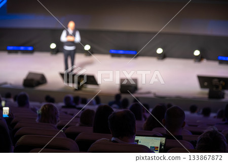 Blurred stage presentation at a conference with a speaker and attentive audience watching intently 133867872