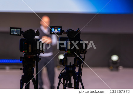 Camera Crew Captures Presenter On Stage During Live Conference With Professional Video Equipment 133867873