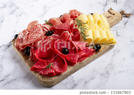 Assorted meat, appetizer, prosciutto, salami and ham, with maasdam cheese and olives, on a wooden board, breakfast, top view, close-up, no people Assorted meat, appetizer, prosciutto, salami and ham, with maasdam cheese and olives, on a wooden board, breakfast, top view, close-up, no people 133867903