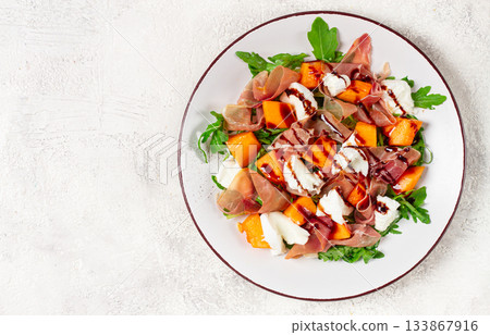 salad with slices of ripe melon, prosciutto, mozzarella and fresh arugula, decorated with balsamic glaze. 133867916