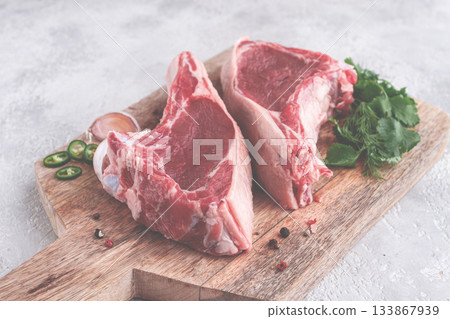 Fresh pieces of beef on the bone, on a wooden cutting board, with herbs and spices, ready for cooking in the kitchen Fresh pieces of beef on the bone, on a wooden cutting board, with herbs and spices, ready for cooking in the kitchen 133867939