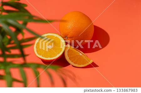 On the coral surface, next to two neatly sliced slices, there is a whole orange. Sunlight casts soft shadows, emphasizing the freshness and bright color of the fruit. On the coral surface, next to two neatly sliced slices, there is a whole orange. Sunlight casts soft shadows, emphasizing the freshness and bright color of the fruit. 133867983