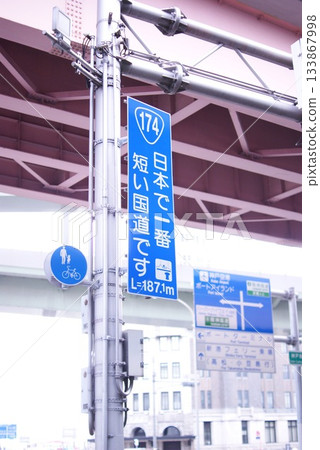 在城市景觀中，一座高架橋橫跨一塊藍色路牌，上面寫著「日本最短的國道」。 133867998