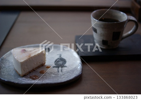 Cheesecake on a ceramic plate with a Japanese pattern and a coffee set by the window 133868023
