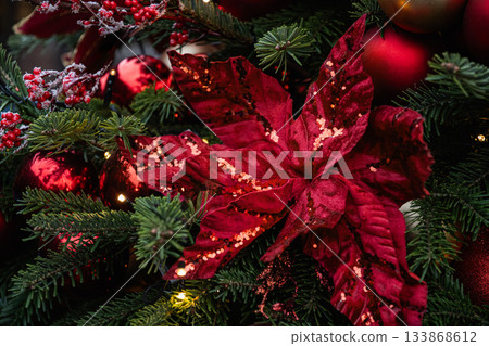 Christmas tree decorated poinsettia and red balls with lights garland. Xmas holiday spirit. Winter. Outdoors. Christmas tree decorated poinsettia and red balls with lights garland. Xmas holiday spirit. Winter. Outdoors. 133868612