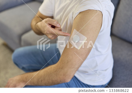 Man pointing at glucose sensor patch on upper arm, wearable diabetes device Man pointing at glucose sensor patch on upper arm, wearable diabetes device 133868622