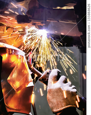 A welder repairs a car's exhaust system, focuses on safety, and uses a burner to cut heated steel in harsh workshop conditions. A welder repairs a car's exhaust system, focuses on safety, and uses a burner to cut heated steel in harsh workshop conditions. 133868626