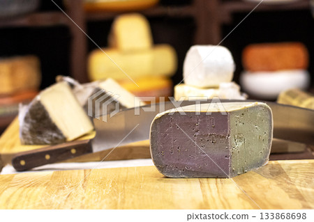 Assorted cheese wheels on a wooden board with a knife in a rustic cheese shop setting 133868698