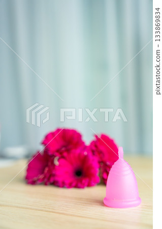 Pink menstrual cup on wooden surface with bright magenta flowers in the background. Aesthetic composition promoting sustainable feminine hygiene and eco-friendly period care. Pink menstrual cup on wooden surface with bright magenta flowers in the background. Aesthetic composition promoting sustainable feminine hygiene and eco-friendly period care. 133869834