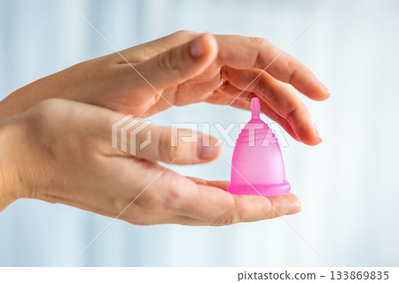 Hands gently holding a pink menstrual cup, symbolizing care, protection, and sustainable feminine hygiene. Concept of eco-friendly period product and body positivity. Hands gently holding a pink menstrual cup, symbolizing care, protection, and sustainable feminine hygiene. Concept of eco-friendly period product and body positivity. 133869835
