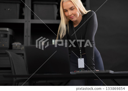 Female IT technician with laptop examining work desk in a tech office setting 133869854