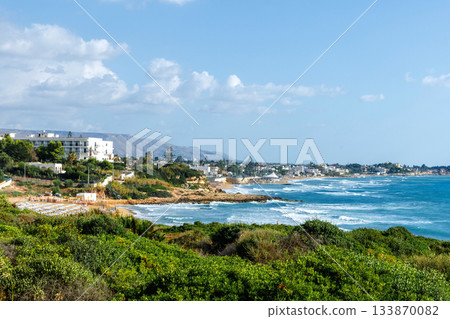 Panoramic Sicilian bay with blue sky green bushes and coastal town 133870082