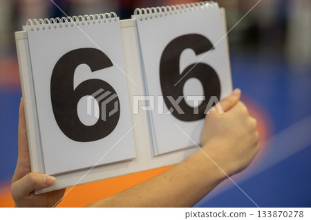 A person's hand holds a white flip scoreboard displaying the numbers 6 and 6 in black digits A person's hand holds a white flip scoreboard displaying the numbers 6 and 6 in black digits 133870278